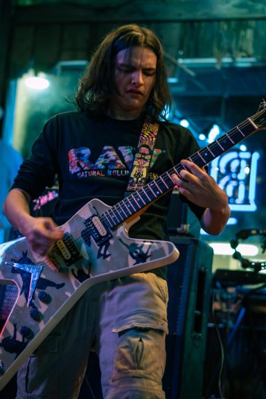 A musician playing an electric guitar on stage in a dimly lit venue.