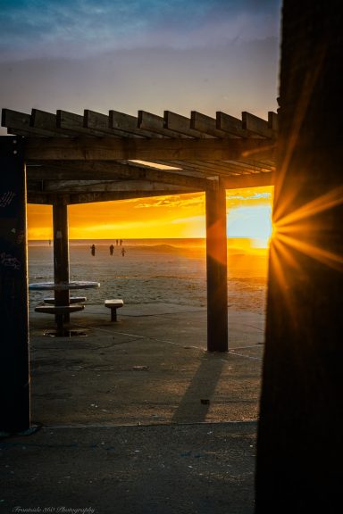 Sunset shining through a pergola at the beach, illuminating shadows on the ground.