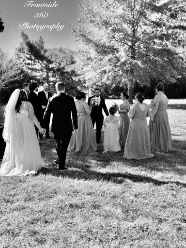 Bridal party walking together in a grassy area, surrounded by trees, in black and white.