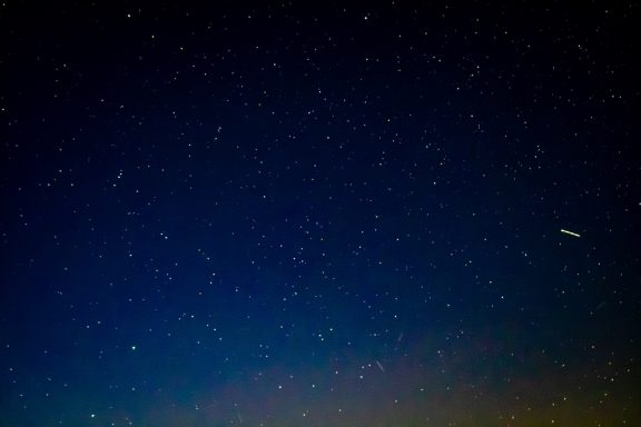 A dark sky filled with numerous stars, with a faint streak of light across the top.