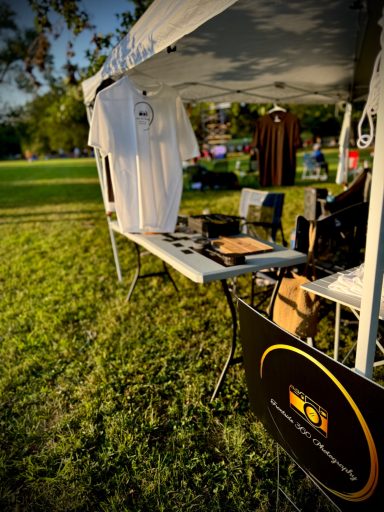 Outdoor vendor setup with merchandise on a table and a banner in a grassy area.